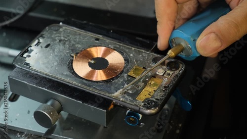 Smartphone repair in a service center, phone secured in a vise while technician removes old adhesive from the frame before installing replacement glass, phone parts and component replacement