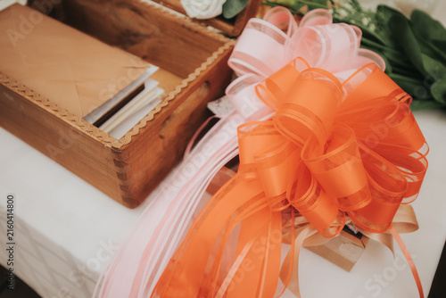 Orange and pink decorative ribbons arranged on a table beside a wooden box containing envelopes and flowers, creating an elegant gift presentation