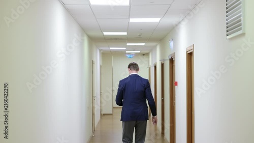 Successful male executive in a formal suit walking through a bright corporate hallway directly towards the camera.Split screen or sequence of a professional businessman walking back and forth in a con