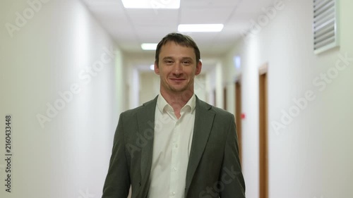 Successful male executive in a formal suit walking through a bright corporate hallway directly towards the camera.Split screen or sequence of a professional businessman walking back and forth in a con