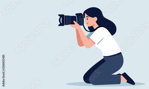 Young woman photographer holding professional dslr camera and kneeling down to take a creative photo on a clean light blue background.