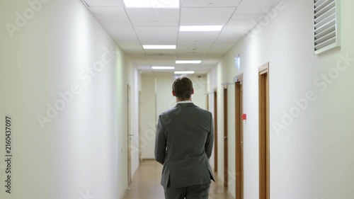 Successful male executive in a formal suit walking through a bright corporate hallway directly towards the camera.Split screen or sequence of a professional businessman walking back and forth in a con