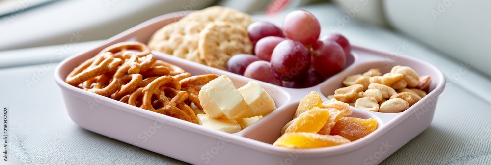 Obraz premium Road trip snack box with pretzels grapes cheese and dried fruit on a car seat for travel banner and snack background