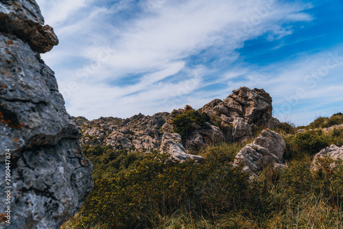 Fotografie rugged limestone mountains and dense mediterranean vegetation under dramatic clouds and blue sky in mallorca, spain