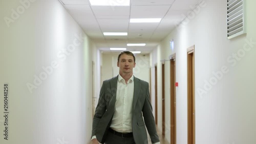 Successful male executive in a formal suit walking through a bright corporate hallway directly towards the camera.Split screen or sequence of a professional businessman walking back and forth in a con