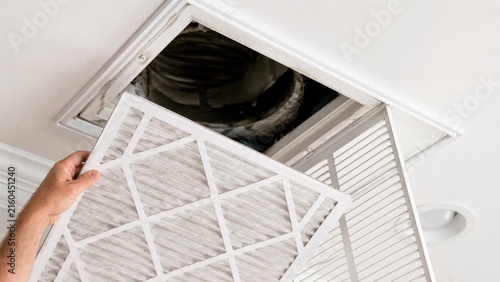 Hand replacing HVAC air filter in a ceiling return vent at home