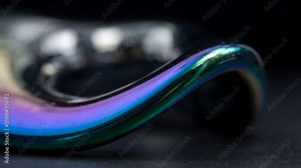 Fototapeta premium Abstract macro shot of iridescent chrome metal with rainbow reflections in purple and green hues on a sleek curved surface against a dark background for futuristic design concepts.