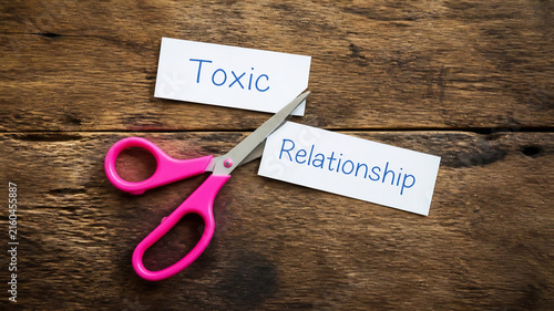 Scissors cutting toxic relationship label on paper. Breaking free from unhealthy partnership with symbolic craft scissors.
