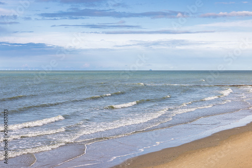 Panoramic view of tranquil sea waves gently breaking on a deserted sandy beach under a soft sky with delicate cloud formations. Ostend town in Belgium, Europe.