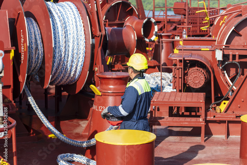 Maritime crew member paying out a mooring rope from a powered mooring winch while preparing the vessel for docking.