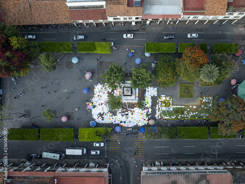 Aerial view of the main plaza in Centro with a central monument, lush green trees, pedestrian walkways, and surrounding streets with traffic in Uruapan, Michoacan, Mexico.