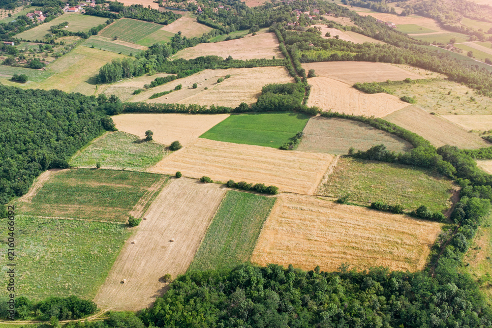 Fototapeta premium Warm golden summer light bathes a patchwork of rolling farmland and a small village nestled among wooded hills. Rural Europe concept.
