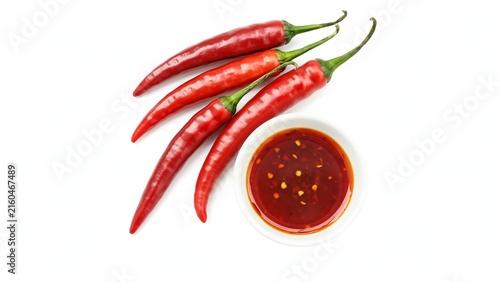 Four bright red chili peppers arranged next to a small white bowl of red chili sauce on a white background
