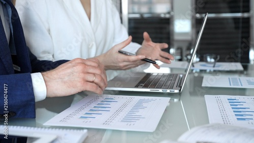 Business professionals in a meeting analyze financial charts and reports on a laptop and documents, pointing at data while planning investment strategy and growth in a modern office