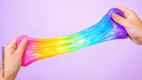Bright rainbow slime being stretched between two hands on a pastel purple background