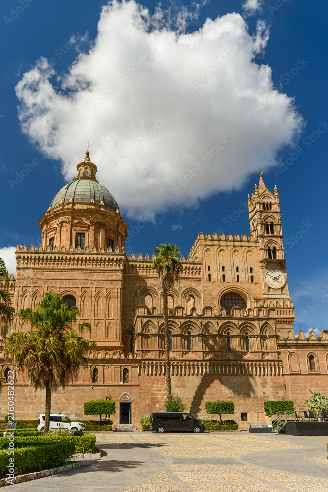 Fototapeta premium Frente de la Catedral de Palermo, en Sicilia. Se observa una torre, el reloj y la cúpula bajo una nube espectacular. Viajando por Italia y el mar Mediterráneo.