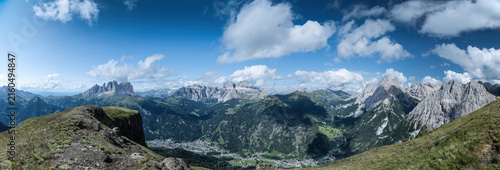 View of the Dolomites landscape featuring Crepa Neigra mountain range overlooking Canazei, with lush green slopes, rocky peaks, and blue sky, Canazei, Trentino-Alto Adige, Italy.