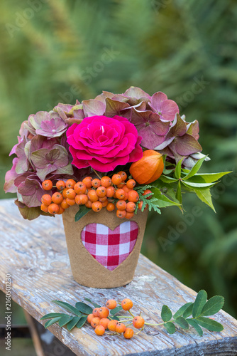Blumenstrauß mit roter Rose, Hortensienblüten, Ebereschen-Beeren und Physalis im Torftopf mit Herzmotiv
