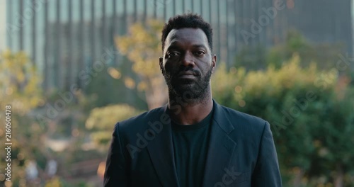 Confident African American businessman poses outdoors near a modern corporate office, making eye contact with the camera in a professional executive portrait.