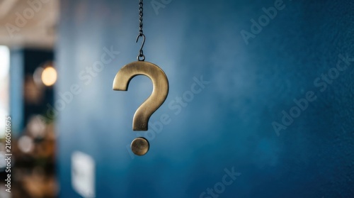 Metal question mark hanging on chain against blue wall