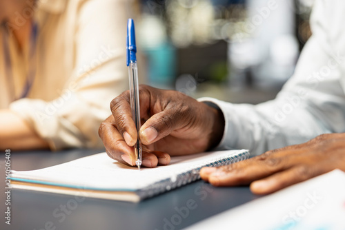 Photography Bookkeeper checks financial reports in the office and writes figures on paper, transcribing information to a notepad with a pen while crosschecking data