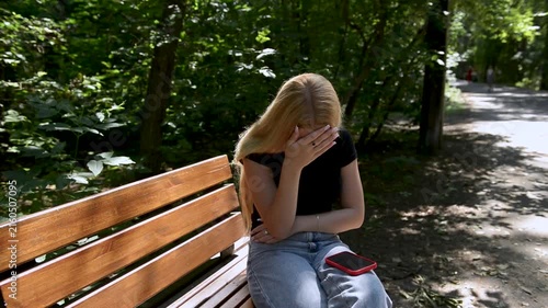 18-year-old girl receives a message and is terribly upset. She lowers her head and clutches it with her hand.