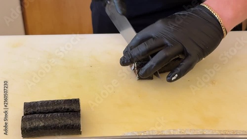 Sushi chef slicing roll on board, Japanese food preparation close up