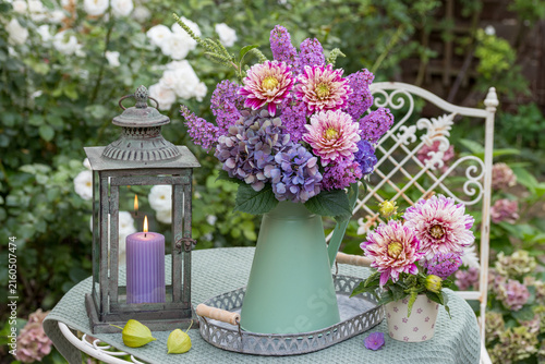 Sommergarten-Arrangement mit Blumenstrauß mit Dahlien, Hortensienblüten und Schmetterlingsbusch-Blüten im vintage Krug und Laterne