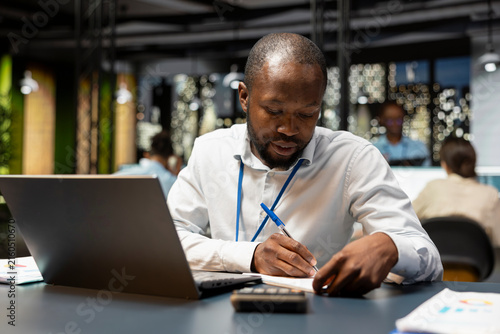 Foto Accountant writes down information in the office late at night, taking notes on paper and documenting research while finishing tedious paperwork before a deadline during overnight work