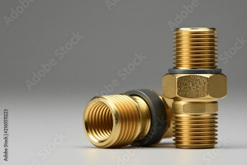 Macro shot of brass compression fittings for industrial piping. Gold metallic connectors with threaded nuts, dark rubber gaskets sit on grey surface. Professional hardware components used for secure