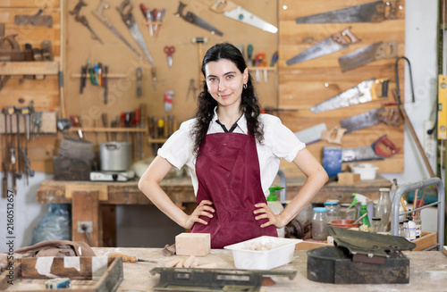 Foto Happy young woman in pinafore standing in taller workroom full of tools