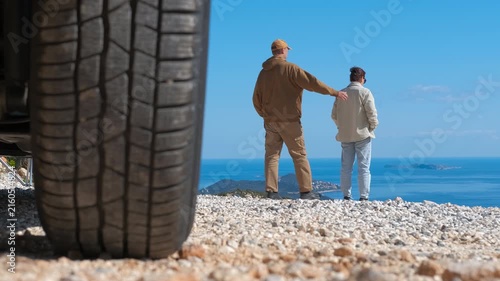 Romantic couple enjoying scenic sea view on a road trip. Couple enjoying a beautiful ocean panorama during a scenic car journey. One man walks up to his partner, puts his arm around him