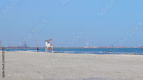 Lifeguard tower on sandy beach with industrial background. Lifeguard tower standing on an empty sandy beach with the sea and an industrial port in the background on a sunny day