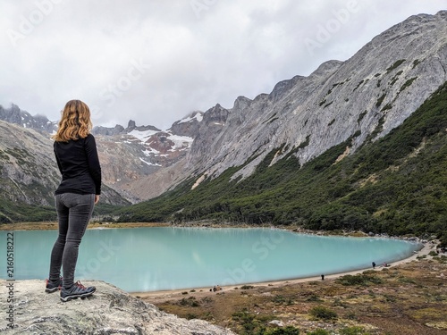 Konstfotografi A woman stands on a rock, back to camera, overlooking the vibrant turquoise waters of Laguna Esmeralda and surrounding snowy mountains, Patagonia, Argentina
