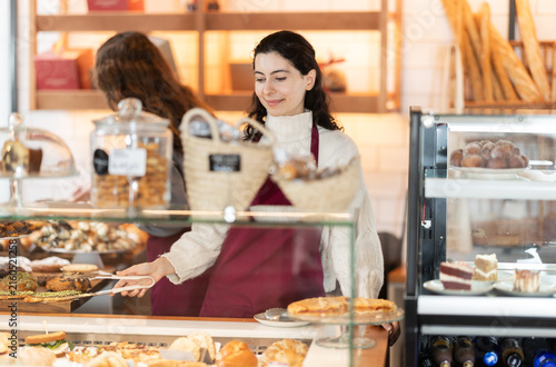 Картината върху платно Young woman seller putting fresh pastries on plate in cafe bakery
