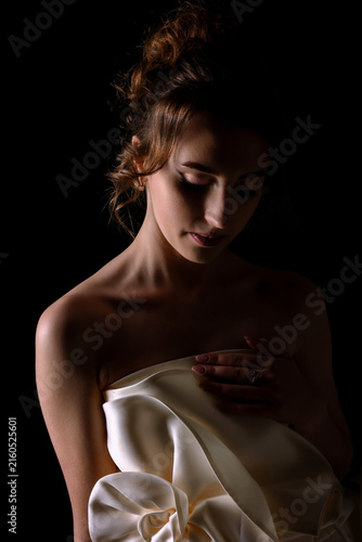 Foto Woman in soft light wearing a white dress holding her shoulder in a dark backgro