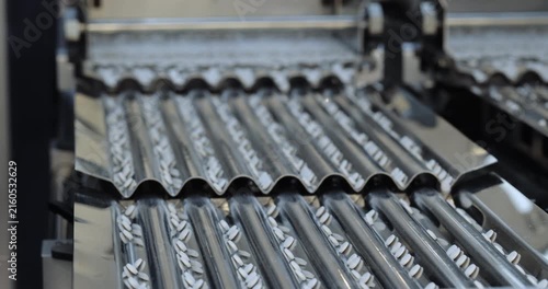 White tablets move along parallel corrugated channels on pharmaceutical line. Automated equipment transports medicine units toward next processing station