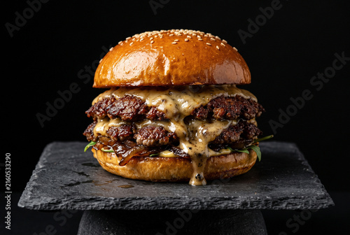 Gourmet double smash burger with crispy beef patties and dripping savory sauce on dark slate board