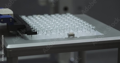 Automatic manipulator takes small glass vials row in lab glassware manufacturing workshop. Modern plant equipment replaces empty bottles for medications