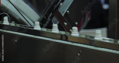 Small opaque bottles travel along high speed conveyor belt in factory workshop. Plastic packaging for medications and cosmetic products at industrial facility