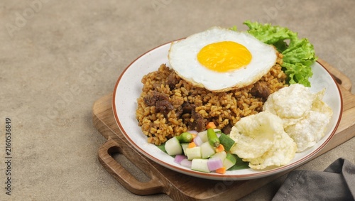 Bild auf Leinwand A plate of fried rice with lamb, fried egg, tomato, shrimp crackers, cucumber and lettuce isolated on wooden textured