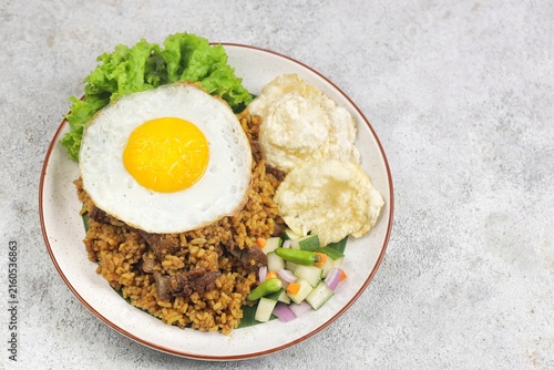 A plate of fried rice with lamb, fried egg, tomato, shrimp crackers, cucumber and lettuce isolated on wooden textured. Nasi Goreng Kambing, indonesian food