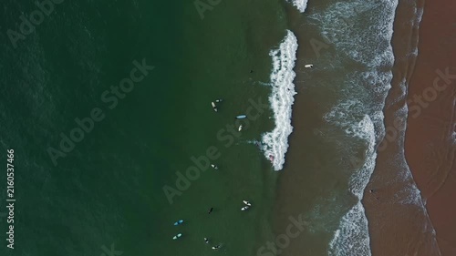 Surfers catch waves and enjoy the ocean at a beach in California on a sunny afternoon. Water is clear and many people are present.