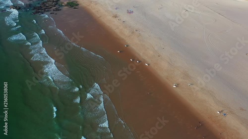 Aerial shots show people walking on beach and waves crashing along the shore in warm daylight aerial view. The sandy coastline stretches endlessly under a clear sky.
