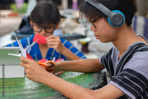 A teenager with headphones focuses on cutting red paper with scissors during a creative craft activity.