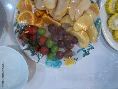 Cuadro en lienzo Colorful assorted fresh fruit platter covered in clear plastic cling wrap, arranged on floral ceramic plate alongside white bowl