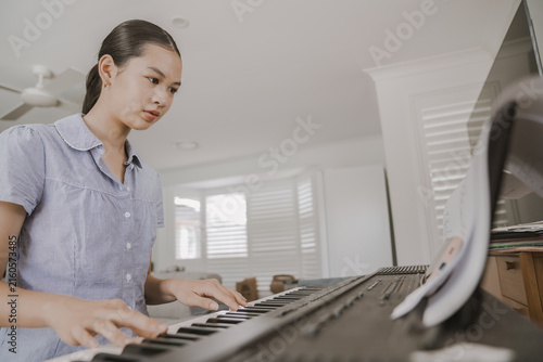 piano, music, teen, home, playing, keyboard, practicing - A young mixed Asian teen focuses on practicing a song on her digital piano in a bright living room, capturing a peaceful moment.