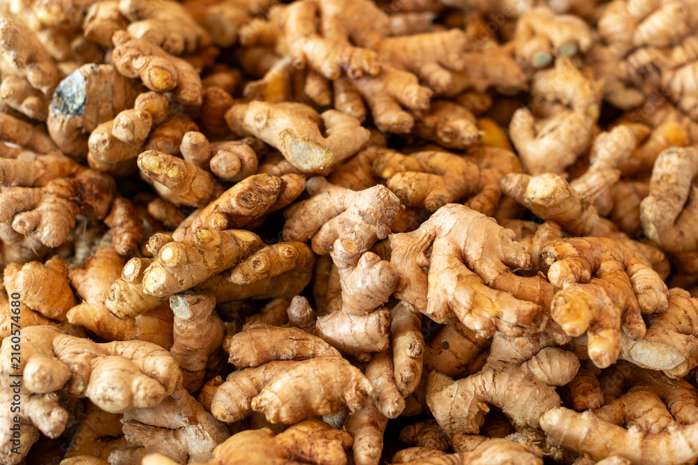 Fototapeta premium Small pieces of organic ginger root piled in a basket at a farmer's market. The small, papery root of a plant is an antioxidant medicine. The skin is tan colored with a yellow center, a rhizome spice.