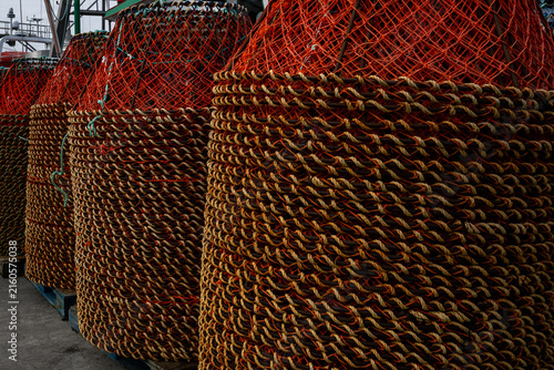 Multiple stacks of industrial crab traps or pots for commercial fishing. The bright orange round nets have metal frames with yellow fishing rope enclosing the edges of the traps. 