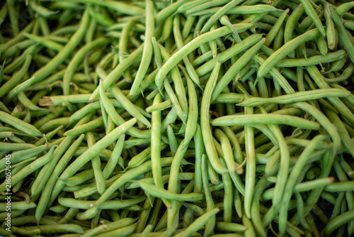 A bin of string beans, asparagus beans, or snap peas is for sale at a farmer's market. The organic green vegetable is a fresh harvest from a farm. The healthy veggie has a waxy pod with cowpeas.